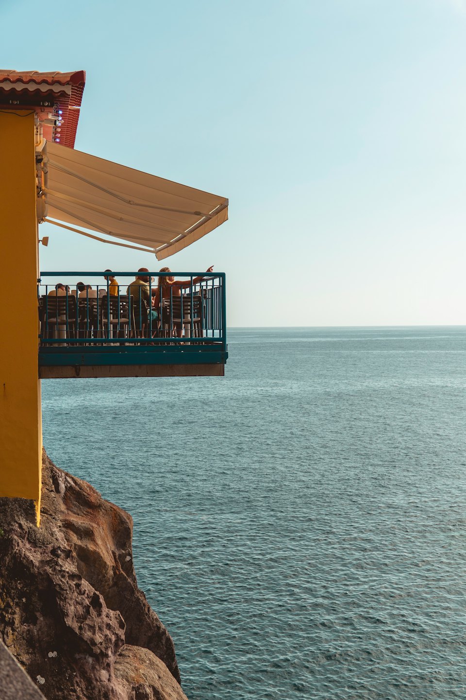 Persone si rilassano sul balcone di un ristorante a picco sul mare, con vista sull'oceano.