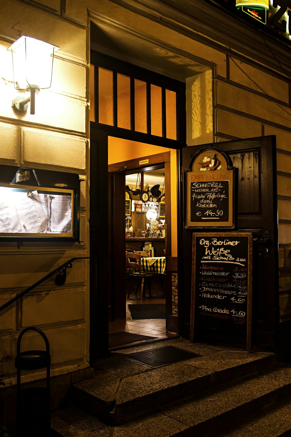 Ingresso di un ristorante di notte con finestre illuminate e menu su lavagna.